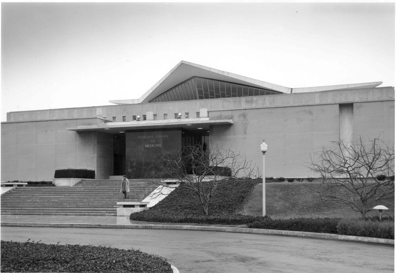 Black and white architectural photo of the entrance to a building with stairs and a road in front of the building