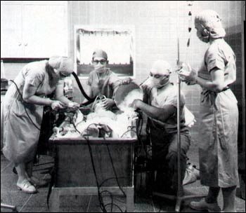 Black and white photo of four people in scrubs and masks in a surgical suite