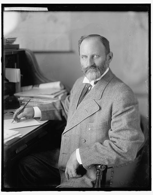 Black and white photo of a main in a suit sitting at a desk