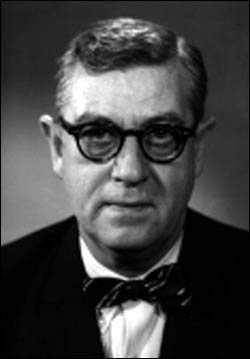 Black and white photo of a man with glasses in a suit with a bowtie