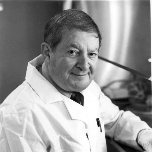 Aurbach, Gerald D in white coat wears a glove and sitting on the chair